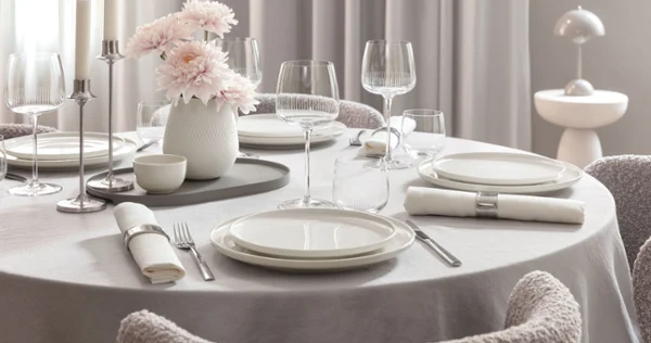 Round dining table with white Afina plates, Afina glasses, cutlery, napkins and a vase with pink flowers.