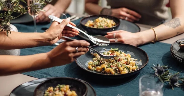 Four people enjoy a meal at one table. Lave bowls with mixed salad are placed on a blue tablecloth. 