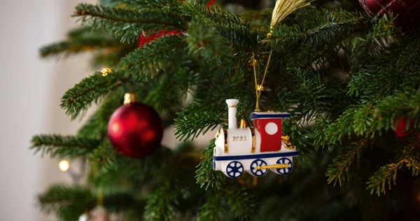 A Christmas tree adorned with a festive train ornament marked "2025" and red baubles. Warm lights add a cozy, cheerful holiday atmosphere.