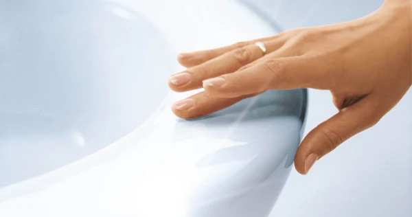 Hand berührt CeramicPlus Toilette Nahaufnahme einer Hand mit einem goldenen Ring, die den Rand eines weißen, glänzenden Keramik-WCs berührt.
