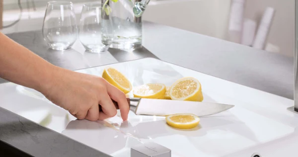En person skär citroner på en vit diskbänk i ett modernt kök.