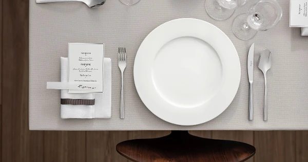 Decorazioni per la tavola per una festa elegante con piatto Royal, carta del menu, posate Piemont e bicchieri visti dall'alto.