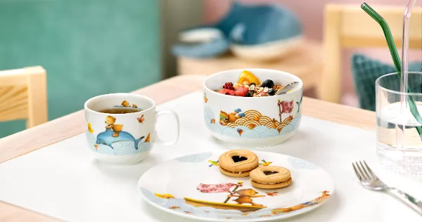 Un ensemble pour le petit-déjeuner Kiddy Bears avec une tasse décorée, une coupe à fruits et une assiette de biscuits sur une table.