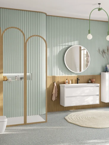 Grande salle de bain familiale vert pastel avec espace douche, meuble-lavabo avec meuble bas blanc, miroir rond éclairé, meuble d'appoint, robinetterie noire et WC suspendu rectangulaire de la collection Skyla.