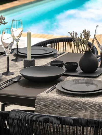 Elegant outdoor dining area with black crockery and glasses from the Manufacture collection beside a pool.