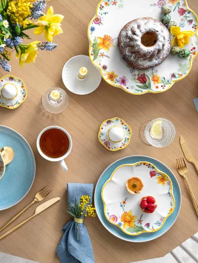 A spring table setting with Spring Awakening and Crafted crockery, a Bundt cake, a bowl of porridge with berries, a cup of tea and decorative eggs.