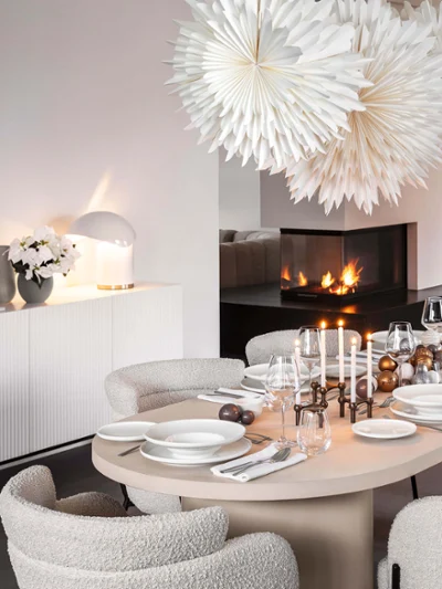 Afina crockery in a modern Christmas ambience A modern dining room set for a meal with white Afina plates and candles. There are also two large paper stars as decorations, a decorated Christmas tree and a built-in fireplace.