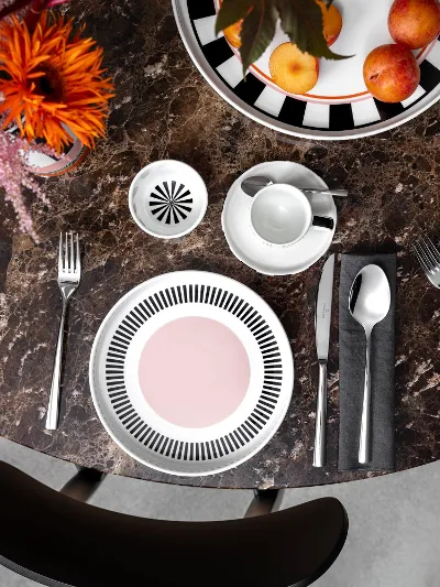 Colour explosion with Memphis by Villeroy & Boch A round marble table with two Memphis place settings, each with a plate, cutlery and a cup. A bowl of apples and a Memphis vase with flowers adorn the center.