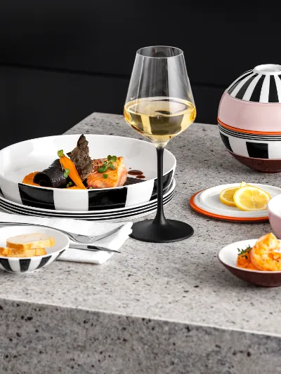 A modernly set table with a glass of white wine, served seafood, sliced bread, and lemon wedges on a granite countertop.