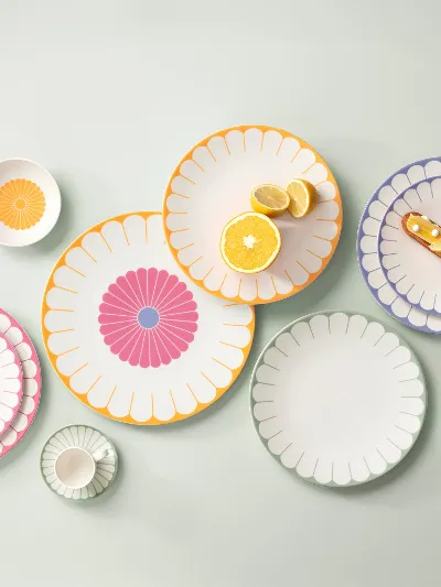 Verschiedene bunte, gemusterte Teller, Schüsseln und eine Tasse sind auf einer hellen Oberfläche angeordnet. Verschiedene bunte, gemusterte Teller, Schüsseln und eine Tasse sind auf einer hellen Oberfläche angeordnet, jeder mit einem anderen Design. Auf einigen Tellern liegt Gebäck.