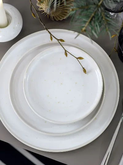 A festive table setting, decorated with Winter Glow plates, cutlery and a Winter Glow candleholder, surrounded by sprigs of fir.