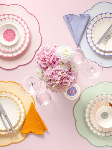 Quattro servizi da tavola dai colori pastello della collezione Fleur con piatti ricurvi, tovaglioli e posate circondano un bouquet di fiori rosa.