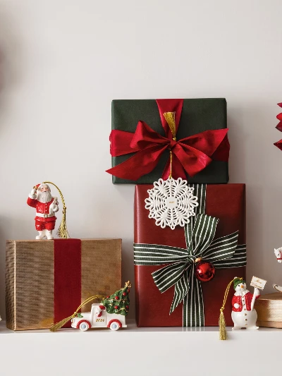 Festive Christmas shelf with wrapped presents, Christmas decorations from Villeroy and Boch, a wreath with red and silver ornaments from Villeroy and Boch and a vase with red flowers and green plants.