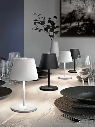 Ein moderner Esstisch mit schwarzen Manufacture Tellern, Gläsern und kleinen Tischlampen, im Hintergrund Kunstwerke und eine Vase.
