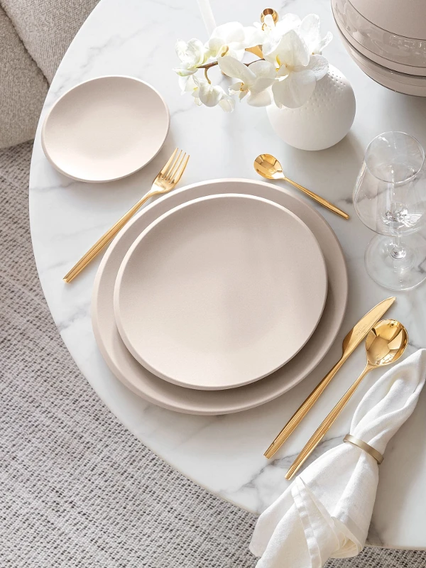 Une table dressée avec des assiettes beige NewMoon et des couverts de table dorés MetroChic de Villeroy & Boch.