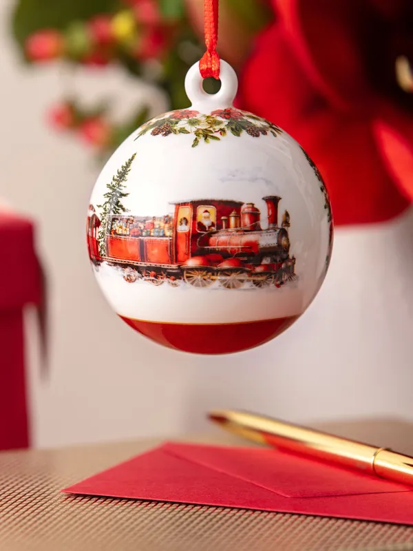 Nahaufnahme eines Weihnachtsornaments mit Zugmotiv, mit eingepackten Geschenken, einem roten Umschlag und einem goldenen Stift im Hintergrund.