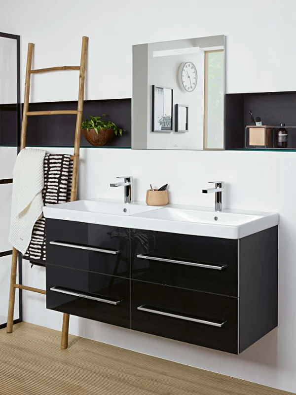 Une salle de bains moderne avec un double lavabo Avento avec des tiroirs noirs, un grand miroir, une échelle en bois avec une serviette blanche, une plante et une horloge au mur.