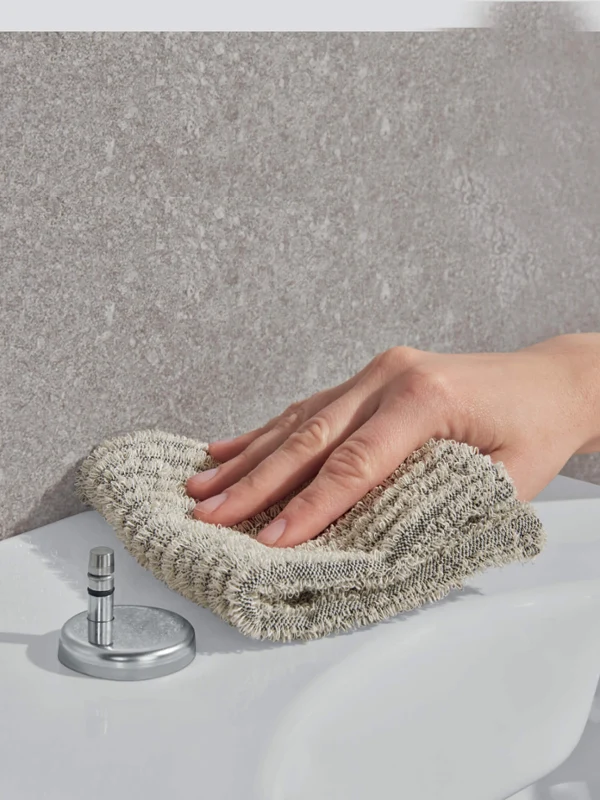 
Eine Person wischt den Rand eines Waschbeckens im Badezimmer mit einem beigen Tuch ab.