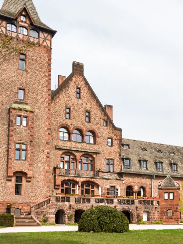 Großes Herrenhaus aus Stein mit einem hohen Turm, umgeben von Grün unter einem klaren Himmel.