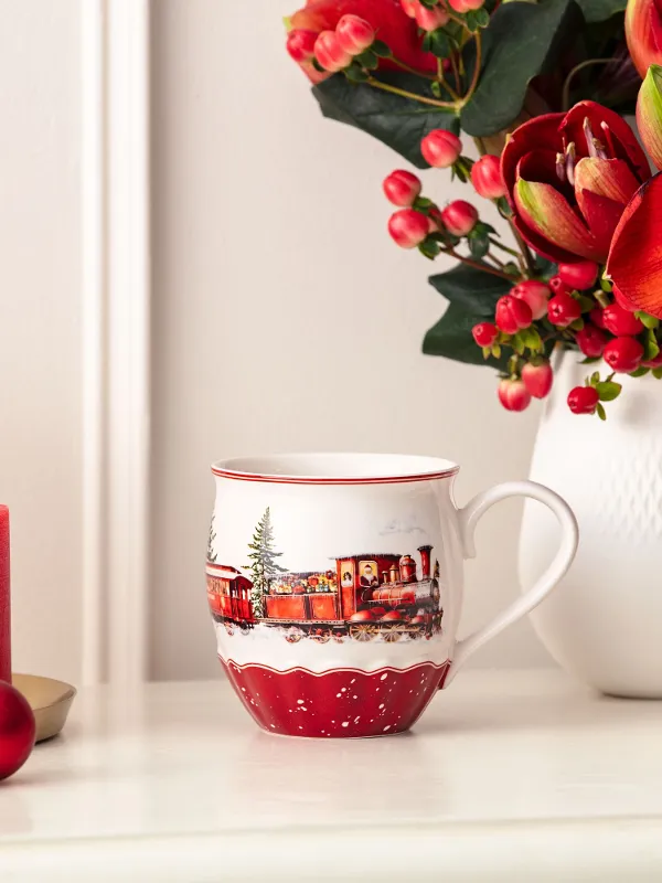 Rote Kerzen, eine festliche Tasse, rote Ornamente und eine Vase mit roten Blumen auf einer weißen Fläche.
