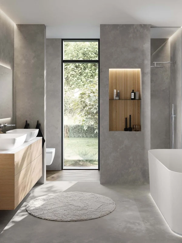 Minimalist bathroom with a Villeroy & Boch Finion bath, a Finion vanity unit and two Artis washbasins. The simple design combines natural wooden elements with modern grey walls and a large window front for a bright, calm ambience.