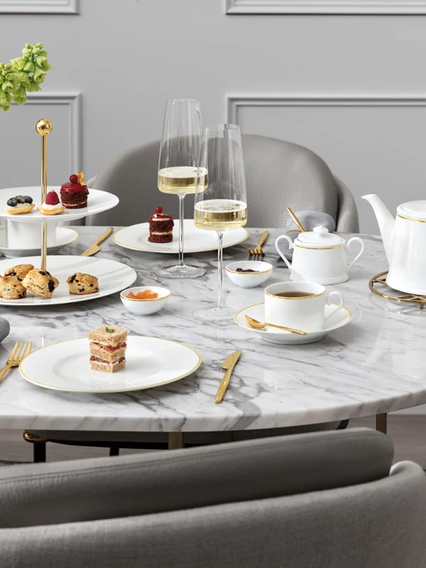Ein für den Nachmittagstee gedeckter Marmortisch mit Desserts, Gebäck, Teeservice, Champagnergläsern und einem Blumenarrangement.