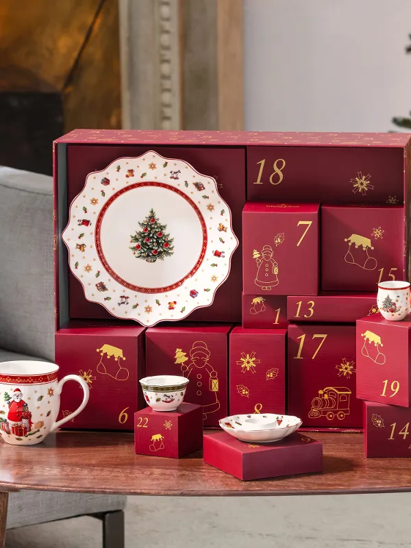 Red Advent calendar boxes and Christmas dishes are placed on a wooden table next to a decorated Christmas tree.