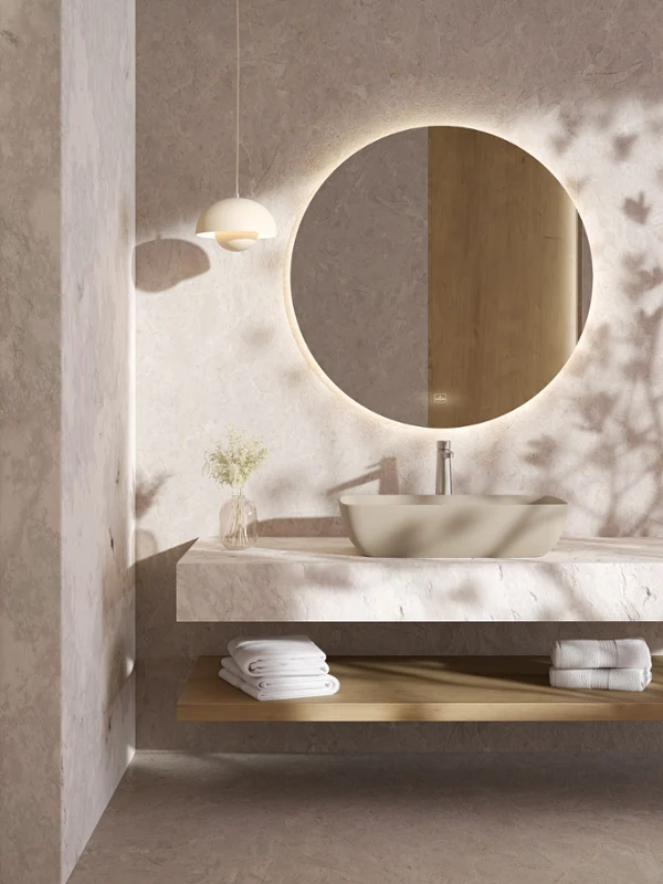 Artis Waschbecken in Marmor-Badezimmer mit rundem Spiegel Minimalistischer Badezimmer-Waschtisch mit rundem, hinterleuchtetem Spiegel, Gefäßwaschbecken, Handtüchern und einer kleinen Vase auf einem schwebenden Regal.
