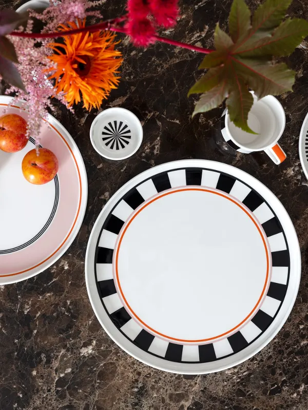 Memphis table setting by Villeroy & Boch with decorative plates, a mug, cups and plums on a brown marble surface decorated with bright flowers.