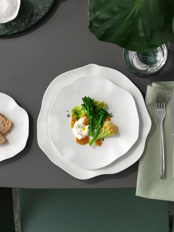 Une assiette Pura avec des légumes et un œuf, une assiette d'accompagnement avec du pain et des couverts sur une serviette posée sur une table grise.