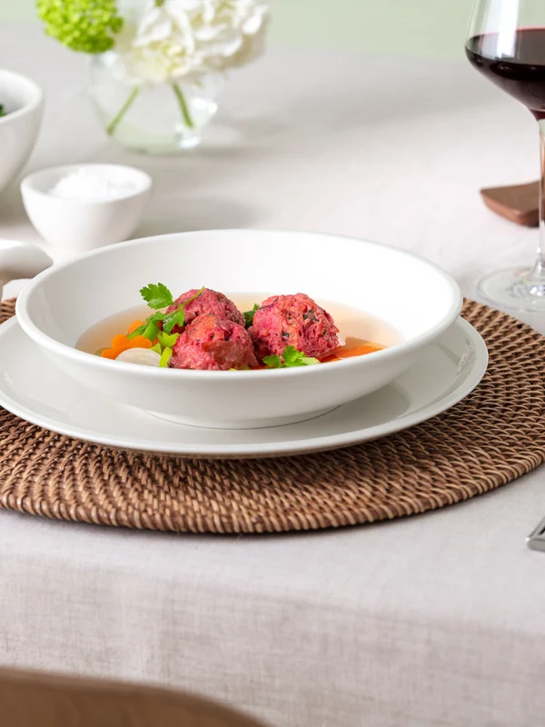 Ein gedeckter Tisch mit einer Artesano-Schüssel mit Suppe, Brot, Salat, einem Glas Wein und Besteck auf einer gewebten Tischset.