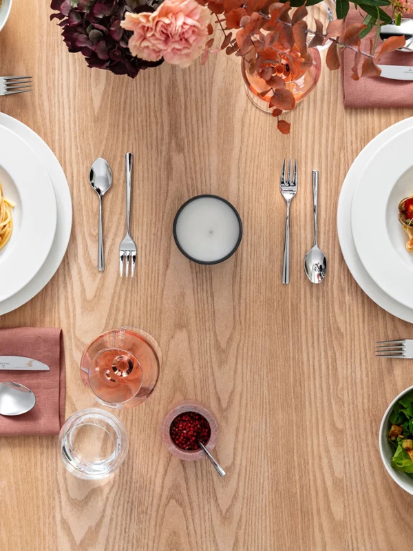 Dining table with two Royal plates of pasta, two salads, cutlery, a candle and a drink. The Villeroy & Boch plates are placed on pink napkins and there is a pink flower arrangement on the table.	