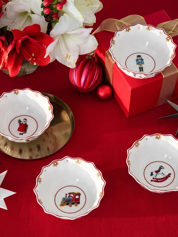 Four decorative bowls from Christmas Toys Memory with Christmas motifs on a red tablecloth, surrounded by ornaments, flowers, and a gift box.