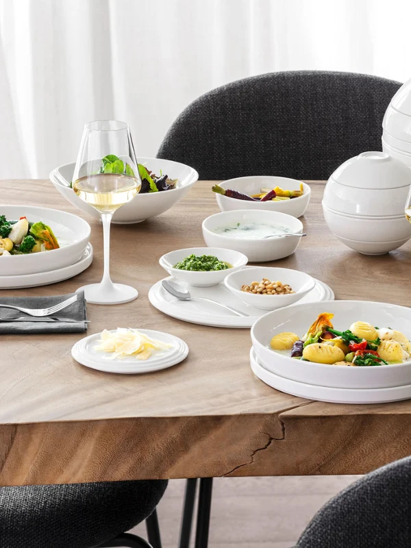 Ein mit La Boule gedeckter Tisch mit zwei Tellern voller Essen, zwei Gläsern Weißwein, verschiedenen Schalen mit Beilagen und einem Blumengesteck mit schwarzen und grauen Stühlen drumherum.