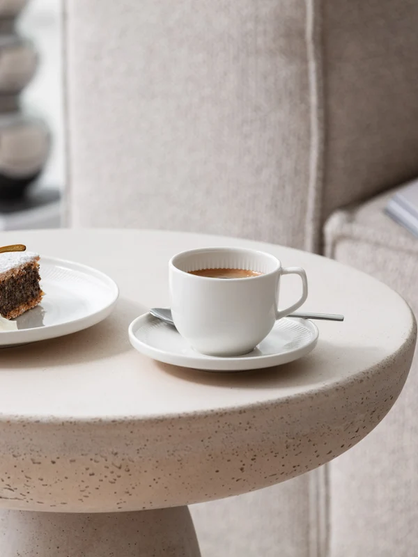 Una tazza di caffè e un piatto di torta serviti su un moderno tavolino con stoviglie Afina di Villeroy & Boch.