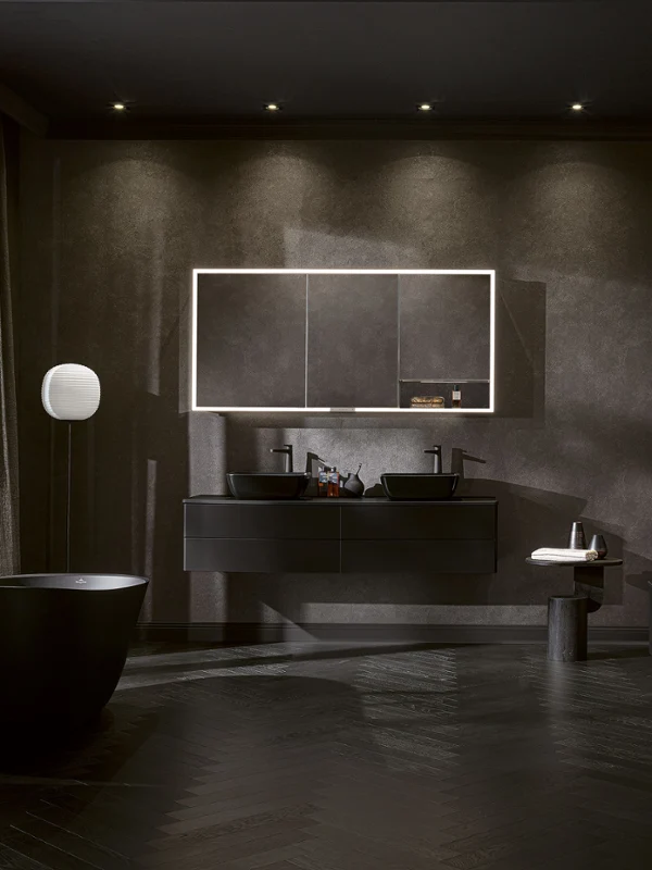 Dramatic Artis all-black bathroom with freestanding bathtub, double vanity, illuminated mirror and soft lighting for a bold and luxurious ambience.
