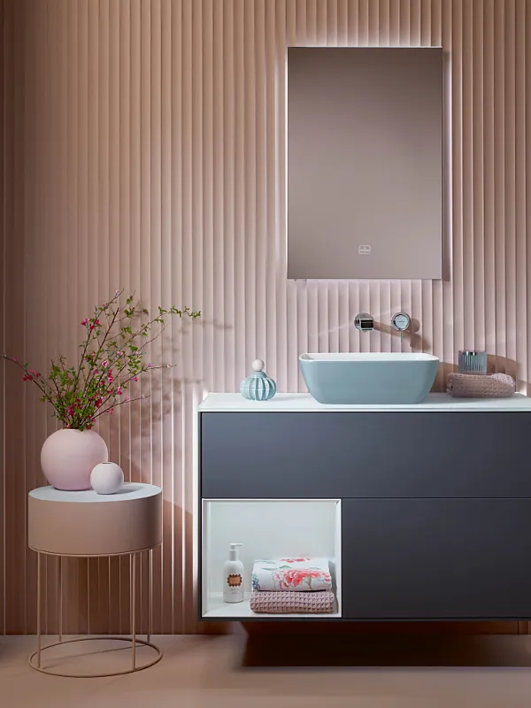 Mobile sottolavabo blu scuro Finion di Villeroy & Boch in un bagno rosa con tavolino rosa.