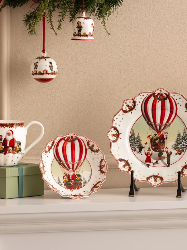 Annual Chistmas edition 2026 collection Festliche Keramikteller, Tassen und Schalen mit Motiven von roten Heißluftballons von Villeroy & Boch werden zusammen mit roten Blumen und Weihnachtsschmuck präsentiert.