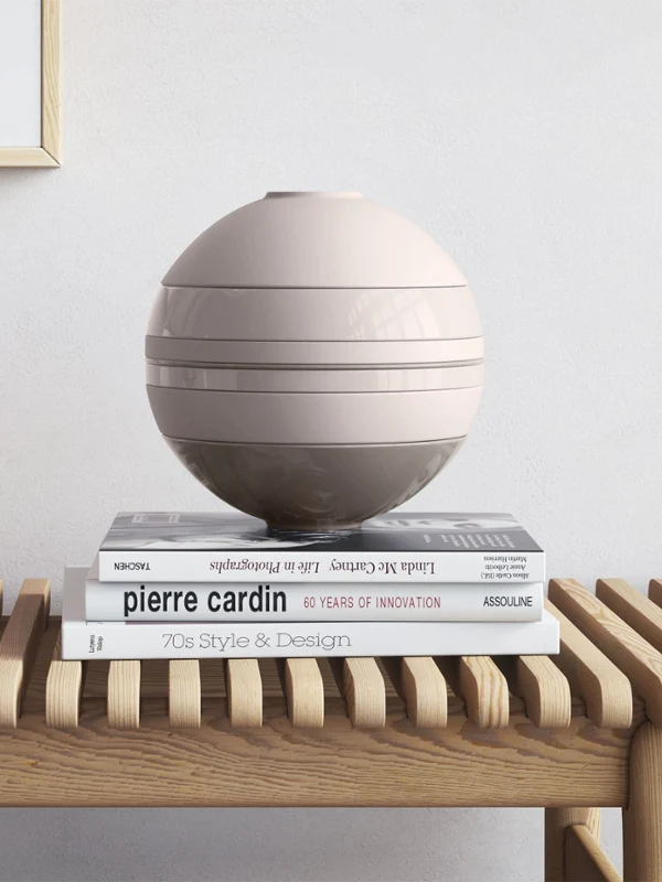 Eine beige La Boule von Villeroy & Boch auf einem Holztisch neben einer Manufacture Vase und Büchern.