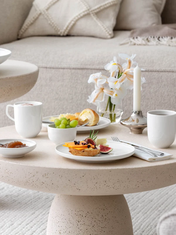 Colazione con caffè, marmellata e panini su un tavolino beige con stoviglie bianche Afina di Villeroy & Boch.