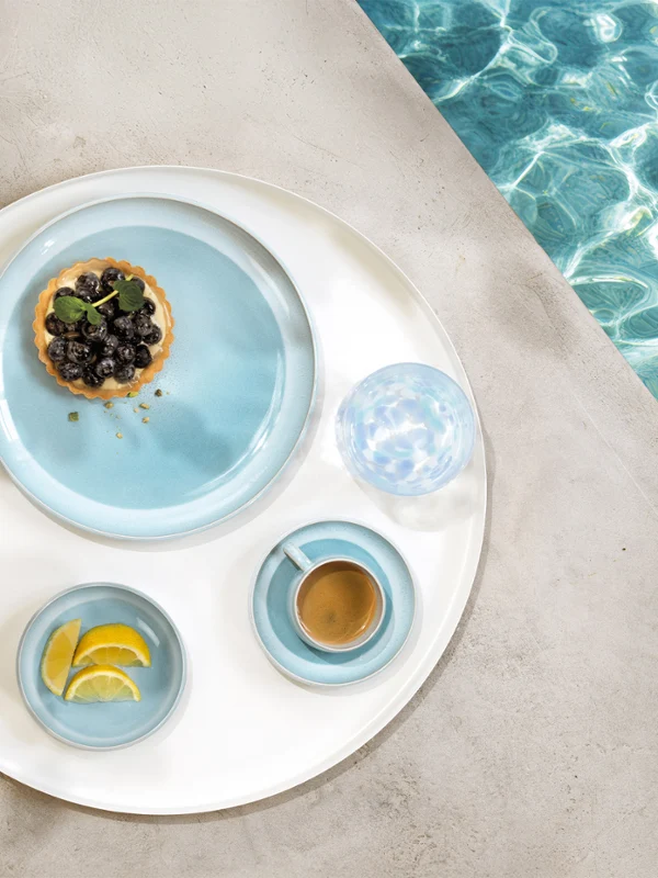 Un plateau rond avec de la vaisselle de la collection Perlemor Aqua et un verre d'eau, au bord d'une piscine.