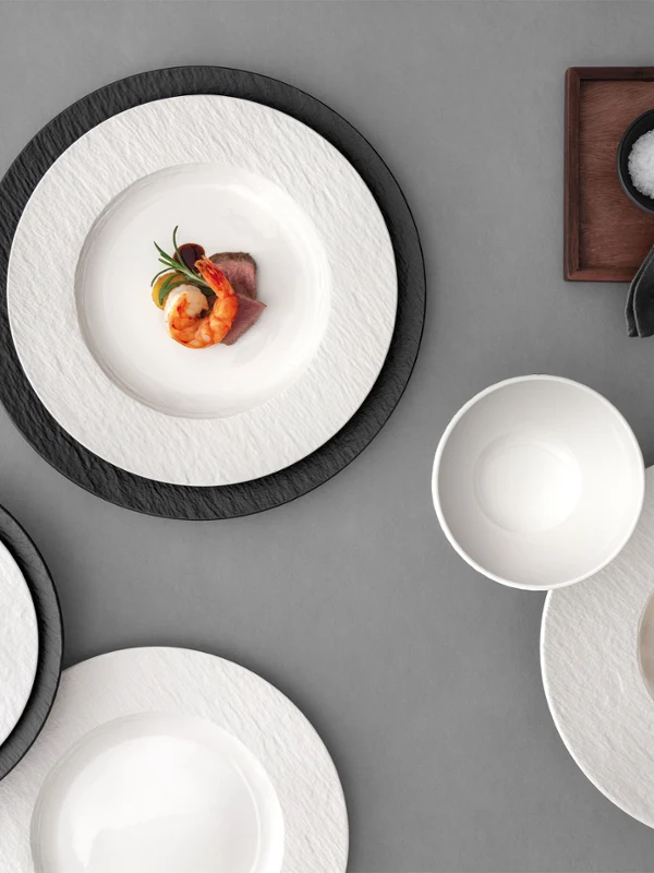 A formal table setting with Manufacture plates A formal table setting with a white and black plates, with food on it on a grey table.