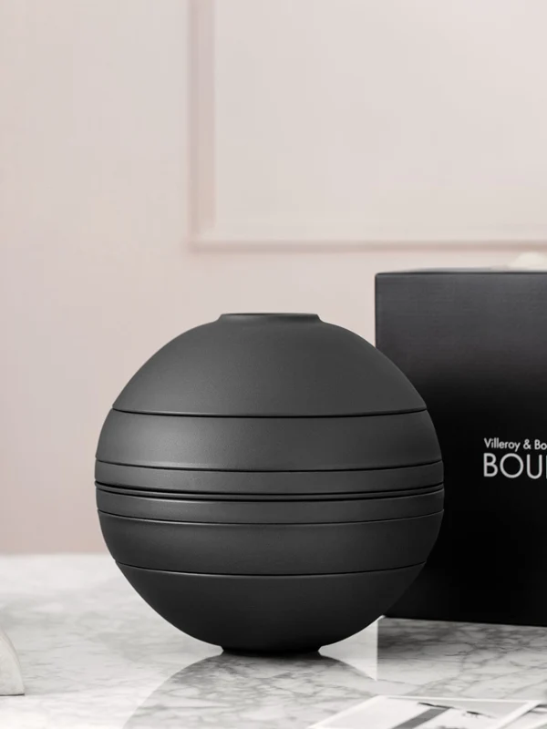 Schwarze La Boule mit Geschenk-Box Ein schwarzes La Boule-Geschirrset auf einem Tisch mit schwarzer Geschenk-Box dahinter.