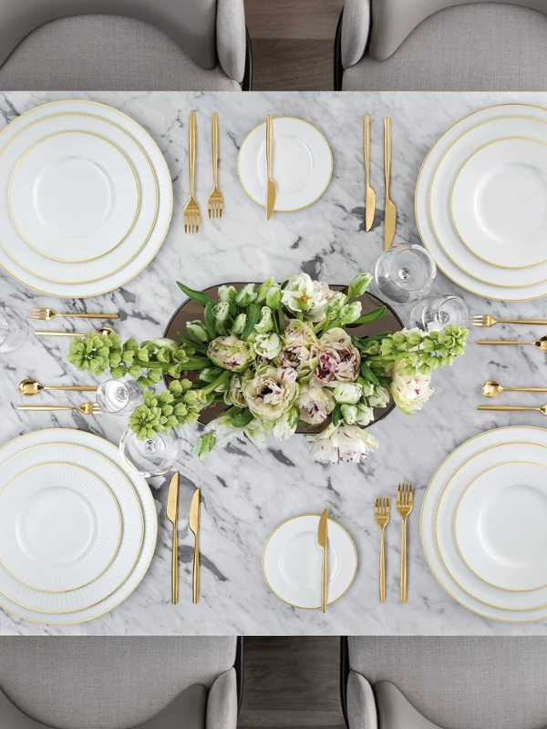 Das Tischset Chateau Septfontaines von Villeroy & Boch ist ein Marmordesign für sechs Personen und elegant mit weißem und goldenem Geschirr, Besteck und Gläsern geschmückt. Ein Blumengesteck mit weißen und rosa Blüten ziert die Mitte, begleitet von kleinen Schalen mit Obst und Nüssen.
