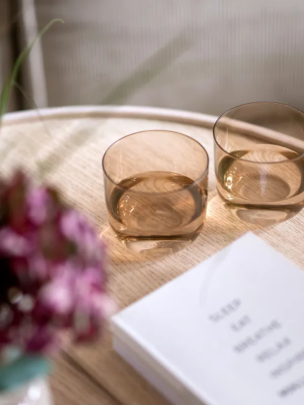 Two Like glasses in orange on a wooden table next to a bouquet of flowers and a book.