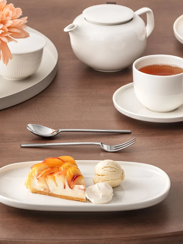 The table set in the Afina collection shows a plate with cake and ice cream, a cup of tea and a teapot on a wooden table with a vase of flowers.
