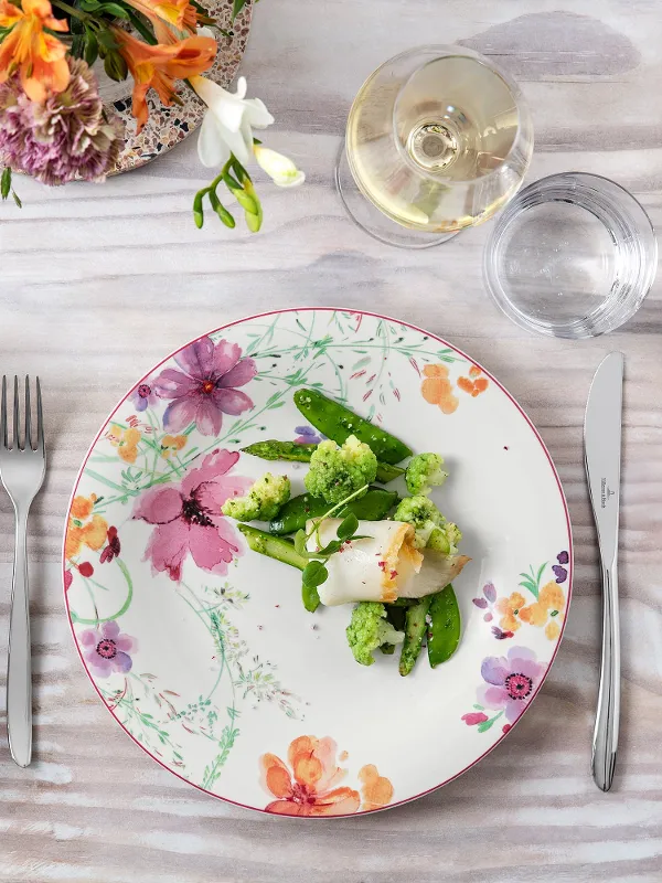 Eleganter Esstisch mit einem Mariefleur Teller mit Blumenmuster, einer gesunden Mahlzeit und einem Glas Weißwein.