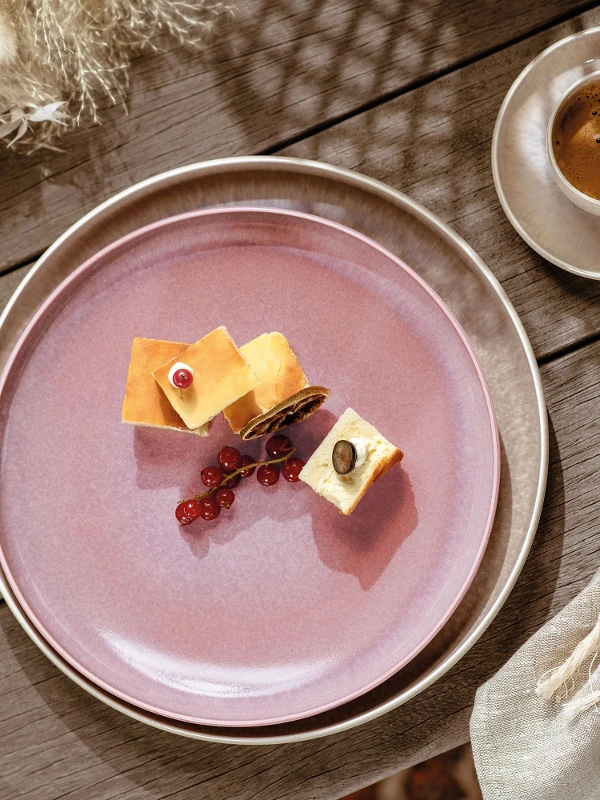 A pink Perlemor breakfast plate from like. by Villeroy & Boch with a piece of cheese and a cup of coffee.