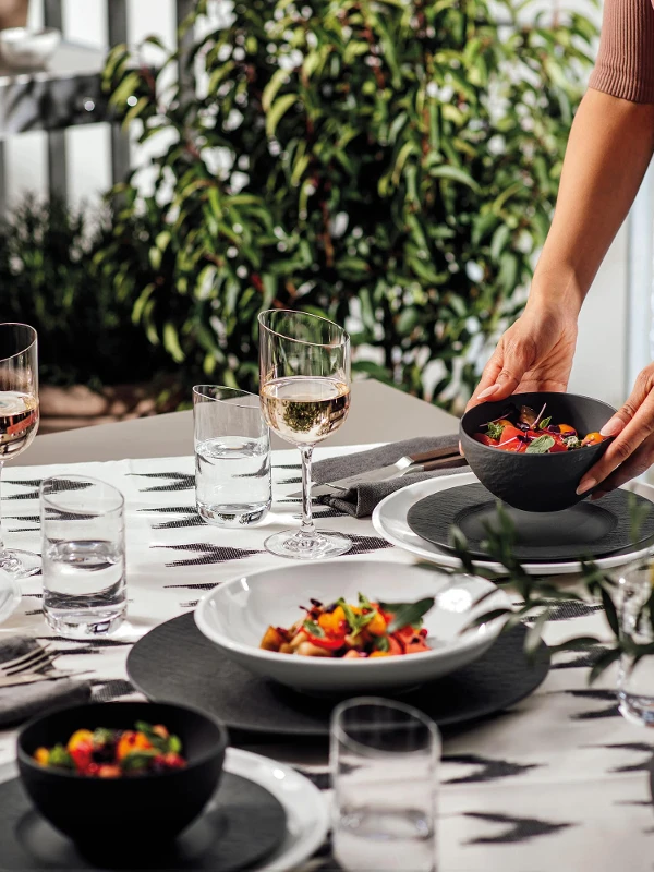 Een vrouw dekt een tafel met NewMoon en Manufacture borden en kommen voor een barbecue-avond buiten.