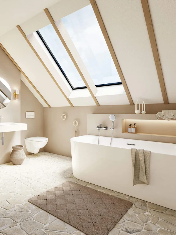 A Loop & Friends bath in a light bathroom with natural stone tiles and a sloping ceiling